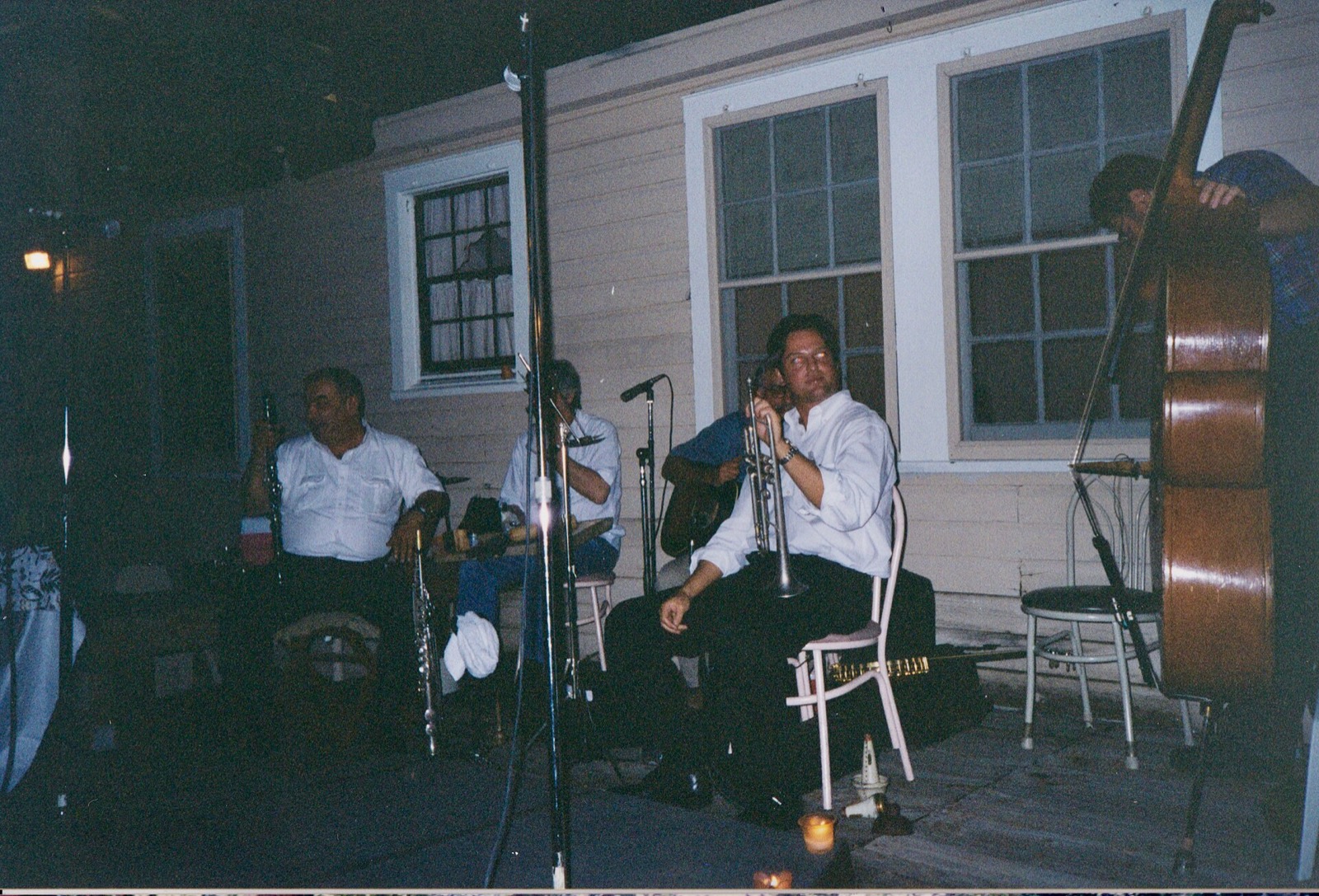Musicians against a clapboard house at night: clarinet, trumpet, guitar, a double bass on the right.