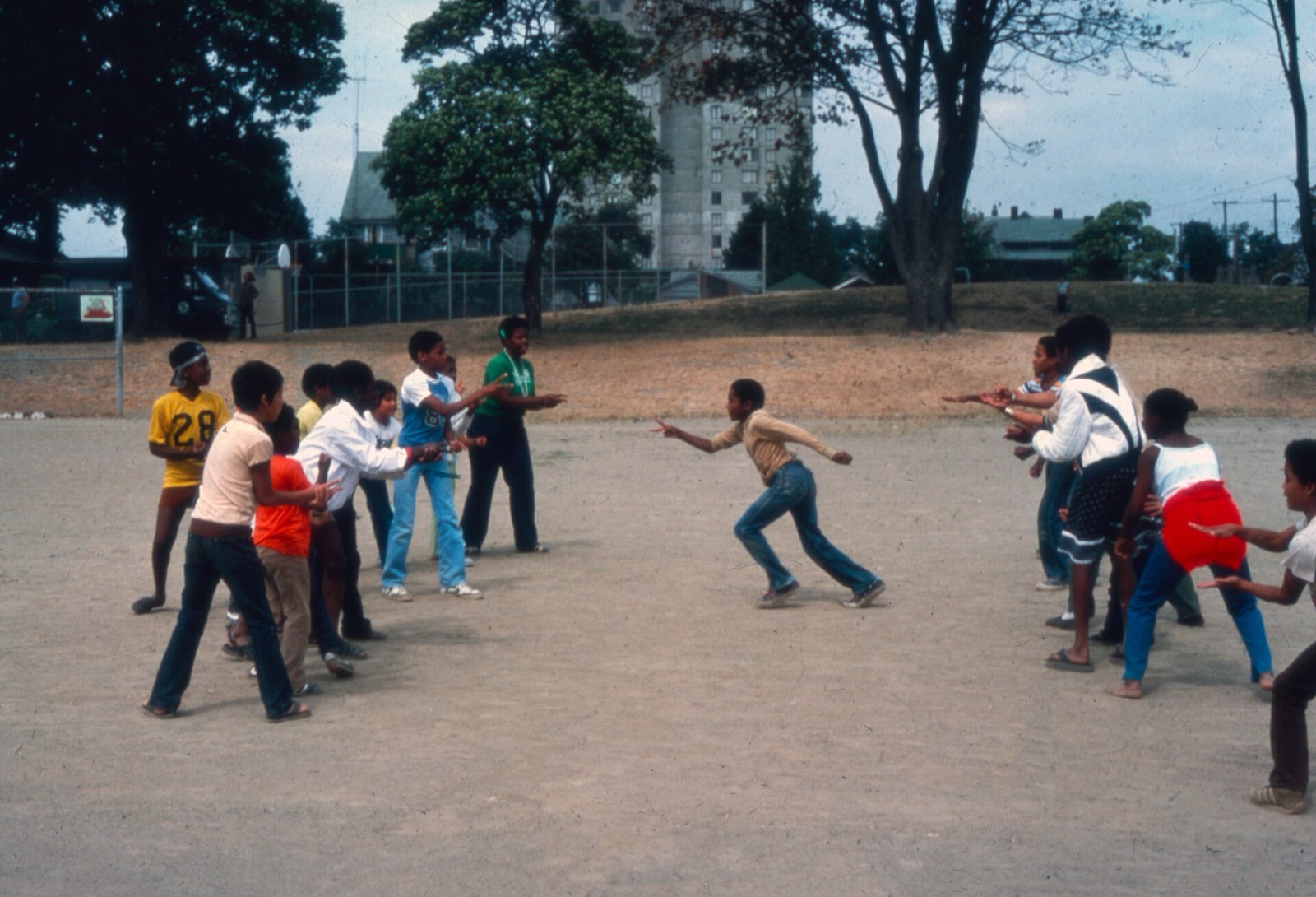Two lines of children facing each other across a dirt field, one boy sprinting between them.